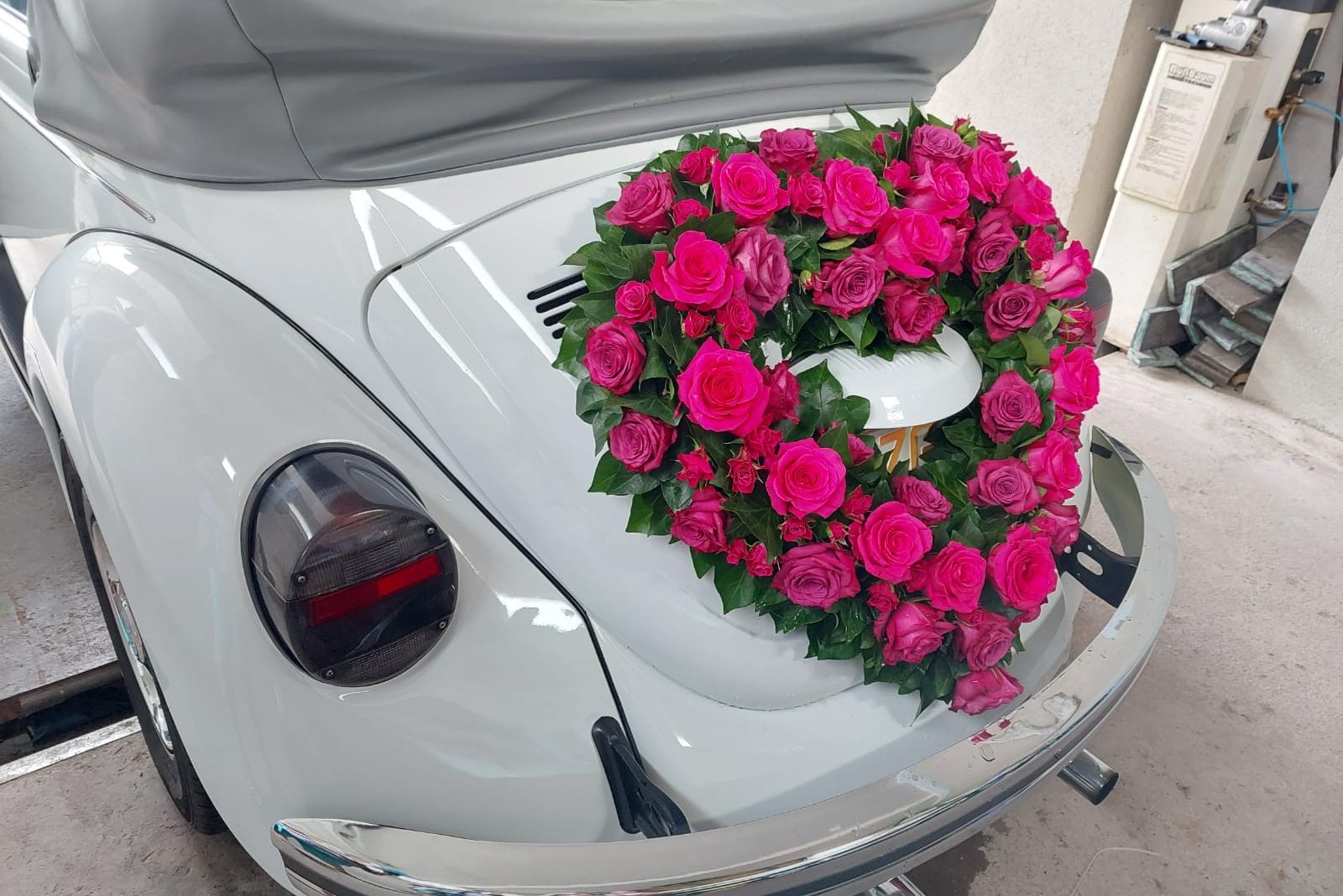 Weißer Käfer mit einer rosafarbenen Blumenkranz-Dekoration auf der Heckklappe.