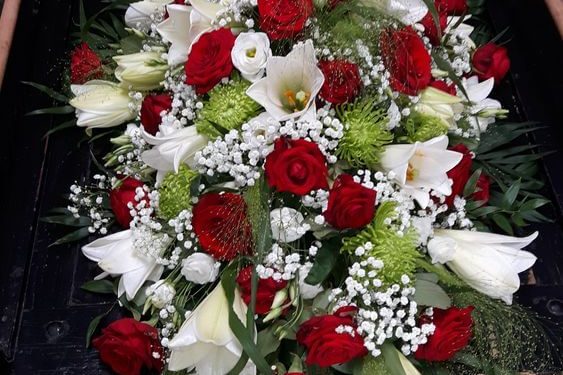 Ein Strauß aus roten Rosen, weißen Lilien und grünem Blattwerk.
